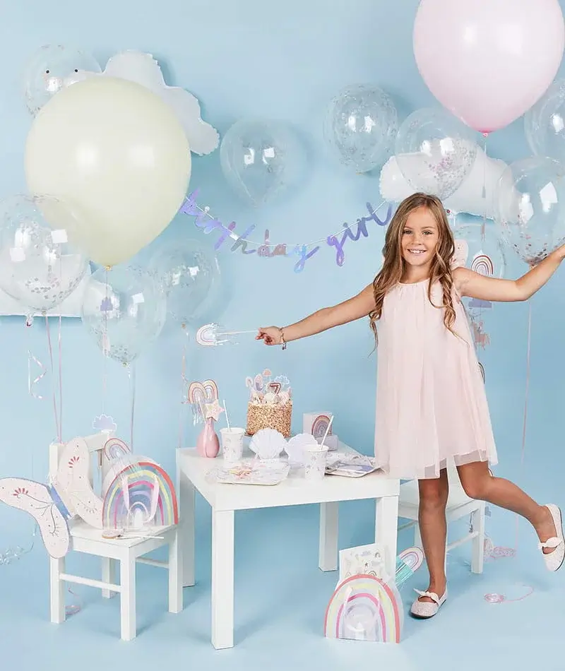 Pastel rainbow-themed party setup with balloons, rainbow decorations, party tableware, popcorn, and a birthday banner. Pastel rainbow-themed party setup with balloons, rainbow decorations, party tableware, popcorn, and a birthday banner.